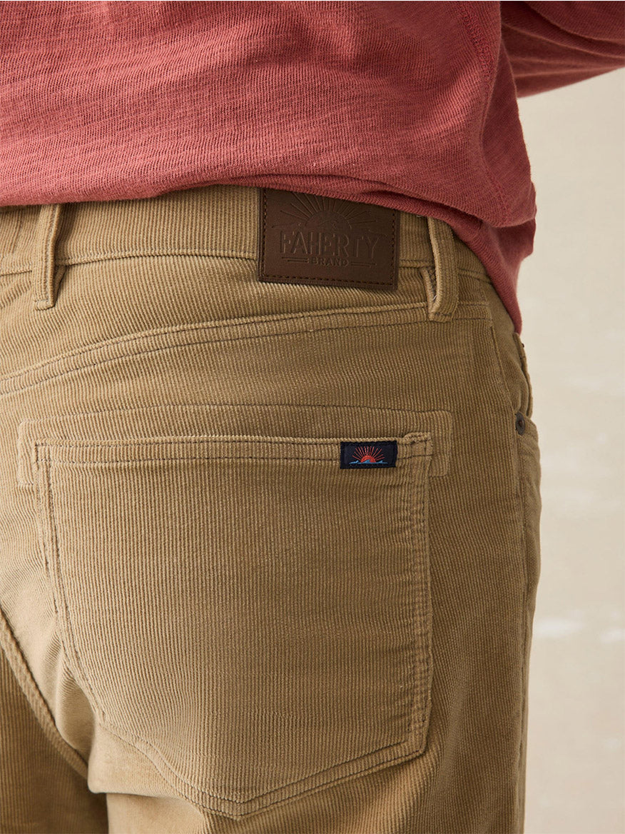 A person wearing the Faherty Brand Stretch Terry 5-Pocket Pant in Barley, crafted from organic cotton, with a brown label on the back pocket, paired with a red long-sleeve shirt.