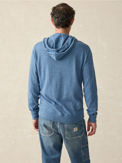 A person dressed in the Faherty Brand Sunwashed Slub Hoodie in Aqua Ocean, made from soft American-grown cotton, and jeans is standing with their back facing the camera.