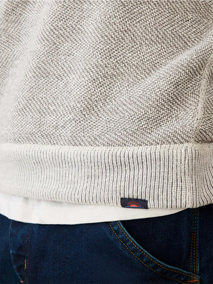 Close-up of the Faherty Brand Whitewater Quarter Zip in Grey Shell Loop, a breathable knit sweater with a ribbed hem, worn over a white shirt and dark blue jeans with visible stitching.