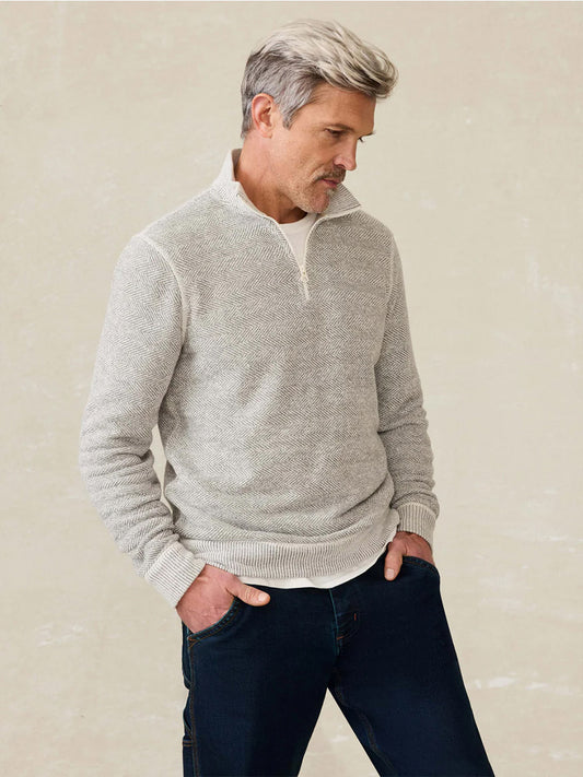 A man with gray hair, hands in his pockets, looks down while wearing dark jeans and a Faherty Brand Whitewater Quarter Zip in Grey Shell Loop.