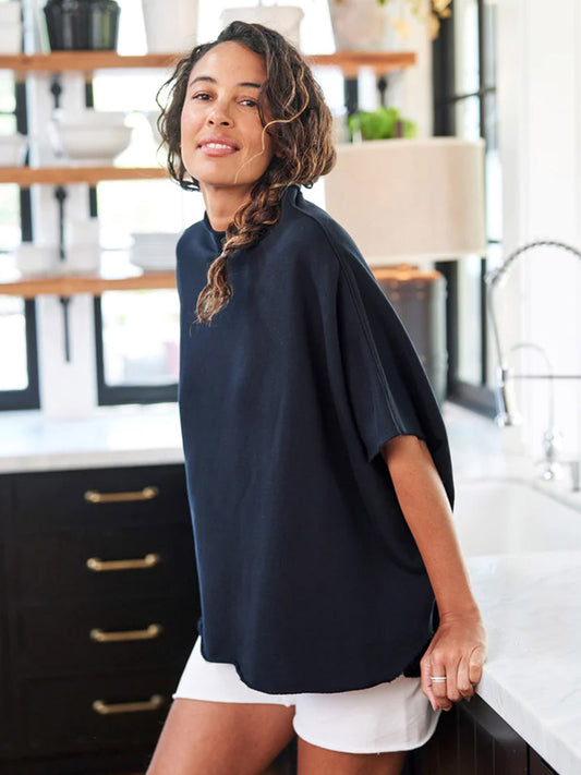 Woman in a casual Frank & Eileen Audrey Funnel Neck Capelet in British Royal Navy Triple Fleece and white shorts smiling in a modern kitchen.