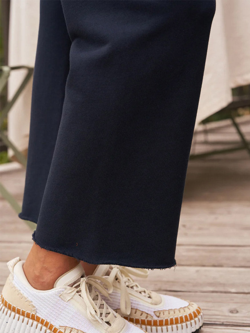 Person wearing white sneakers with a raised, textured sole, and the Frank & Eileen Catherine Favorite Sweatpant in British Royal Navy Triple Fleece with a frayed hem.