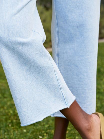 Close-up of a person standing on grass wearing Frank & Eileen Catherine Favorite Sweatpant in Mineral Blue Triple Fleece with wide legs, cropped unfinished hems, and beige shoes.