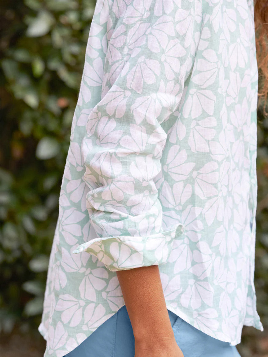 Close-up of a woman's arm draped in a Frank & Eileen Eileen Relaxed Button-Up Shirt in Mint Floral Classic Linen, set against a background of dense foliage, capturing a casual California vibe.