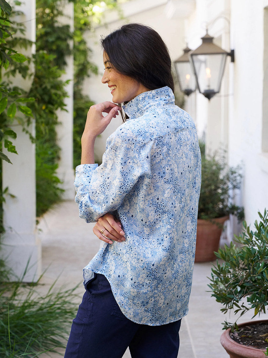 Side view of a person with long hair wearing a Frank & Eileen Eileen Relaxed Button-Up Shirt in Blue Floral and dark pants, exuding California effortlessness on a plant-lined path with lanterns.