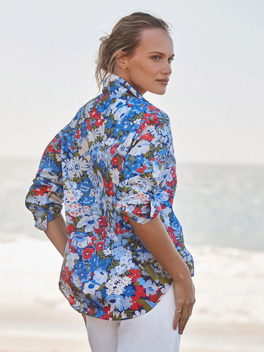 Woman standing on a beach, facing away, wearing the Frank & Eileen Eileen Relaxed Button-Up Shirt in Blue & Red Floral with bust-flattering button placement and rolled sleeves, paired with white pants—effortless California style.