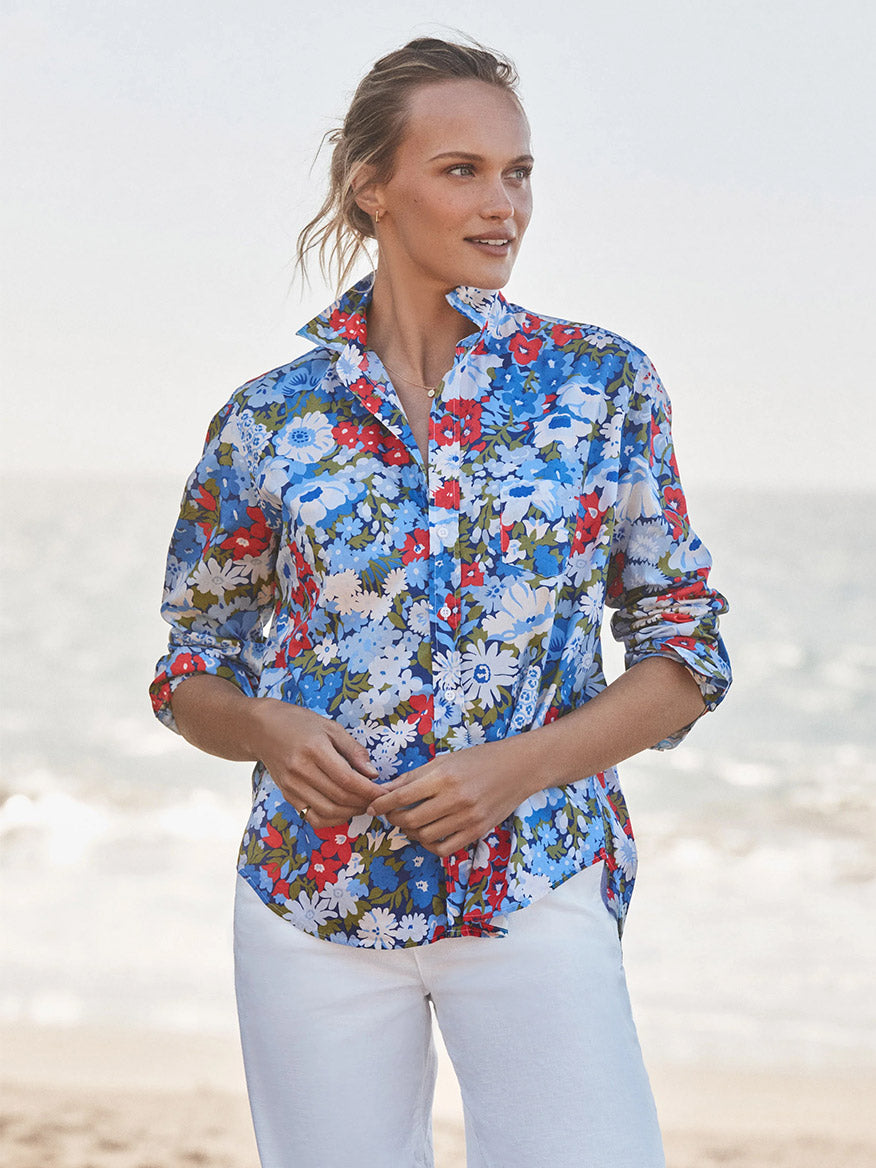 Person stands on a beach in the Frank & Eileen Eileen Relaxed Button-Up Shirt in Blue & Red Floral and white pants, gazing to the side with the ocean behind them—effortlessly channeling casual California style.
