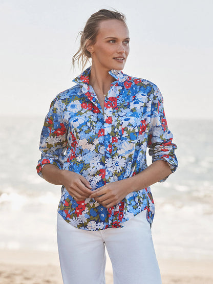 Person stands on a beach in the Frank & Eileen Eileen Relaxed Button-Up Shirt in Blue & Red Floral and white pants, gazing to the side with the ocean behind them—effortlessly channeling casual California style.