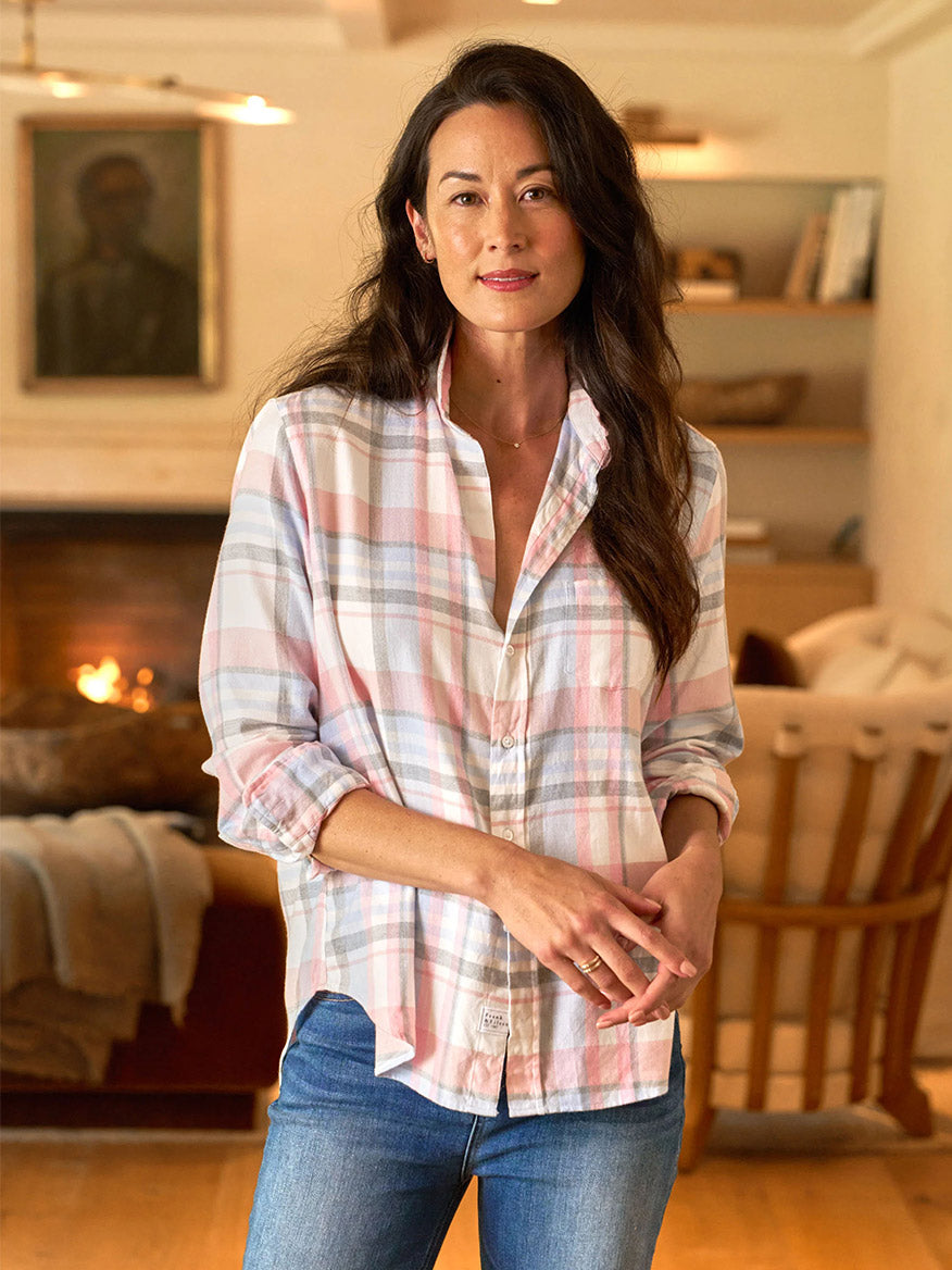 Wearing a Frank & Eileen Eileen Relaxed Button-Up Shirt in Pink & Blue Gray Plaid, someone stands in a cozy room with fireplace warmth and charming bookshelves, exuding California effortlessness in a bust-flattering plaid.