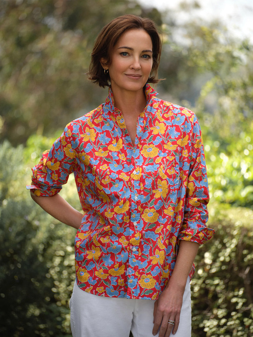 A woman stands outdoors in the Frank & Eileen Eileen Relaxed Button-Up Shirt in Red Flowers, styled with white pants for a casual California look. Her short brown hair frames a slight smile as she poses with one hand in her pocket.