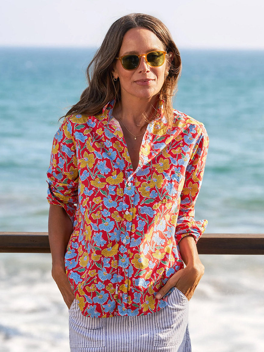 Wearing the Frank & Eileen Eileen Relaxed Button-Up Shirt in Red Flowers, a woman in sunglasses stands by the ocean, hands in her pockets, showcasing effortless California style.