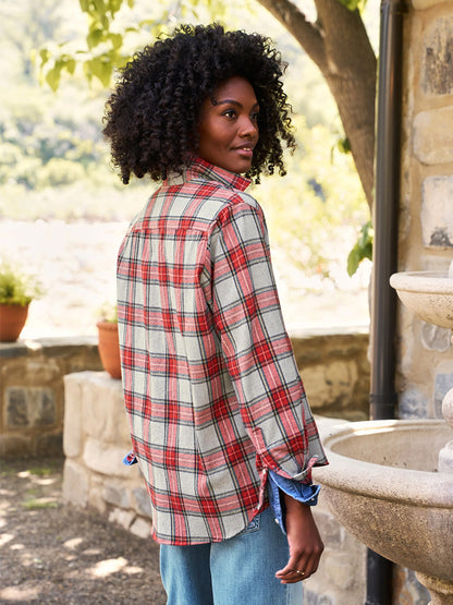 Wearing the Frank & Eileen Eileen Relaxed Button-Up Shirt in Red & Grey Plaid paired with jeans, a person stands outdoors near a stone wall and plants, casting a glance over their shoulder while capturing the cozy essence of Fireside Warm Flannel.