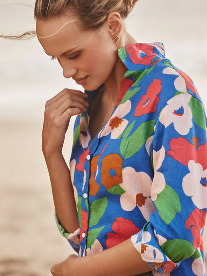 Wearing the Frank & Eileen Mary Classic Shirtdress in Bright Blue Floral, a person stands outdoors looking down gently—a true wardrobe must-have.