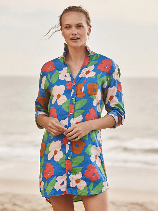 A person stands on the beach wearing the Frank & Eileen Mary Classic Shirtdress in Bright Blue Floral—a bold, colorful piece that's a true wardrobe must-have.