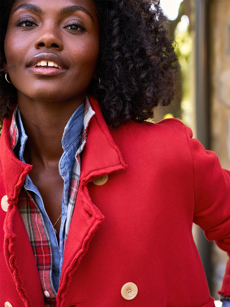 A person wearing the luxurious Frank & Eileen Mini Belfast Crop Peacoat in Crimson Triple Fleece, adorned with horn buttons, and a plaid shirt underneath stands outdoors, slightly smiling.