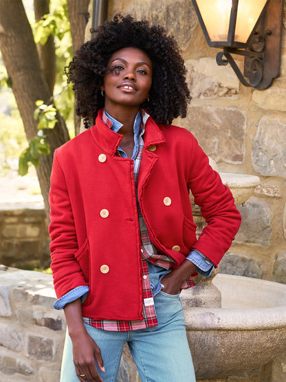 A person stands outdoors near a stone wall and lantern, wearing the Frank & Eileen Mini Belfast Crop Peacoat in Crimson Triple Fleece over a layered plaid shirt and denim jeans.