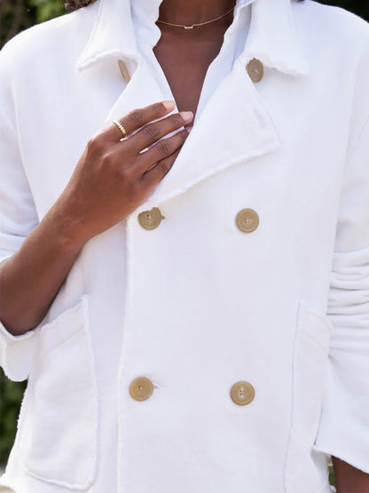 A close-up of a person's hand adjusting a Frank & Eileen Mini Belfast Crop Peacoat in White Triple Fleece, showing detailed buttons and rings on their fingers.