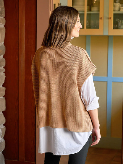 A woman stands indoors facing away, wearing a white button-down shirt under the Frank & Eileen Montecito Italian Sweater Vest in Camel.