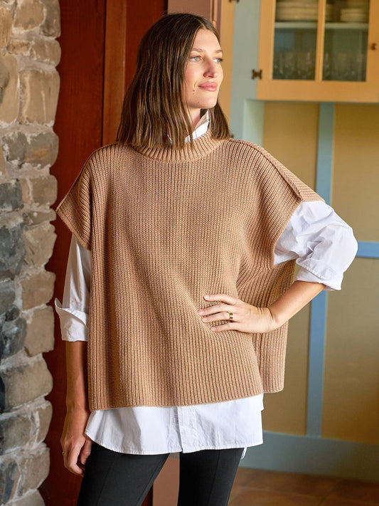 Indoors, a woman looks to the side wearing the Frank & Eileen Montecito Italian Sweater Vest in Camel, layered over a white button-down shirt and black pants.