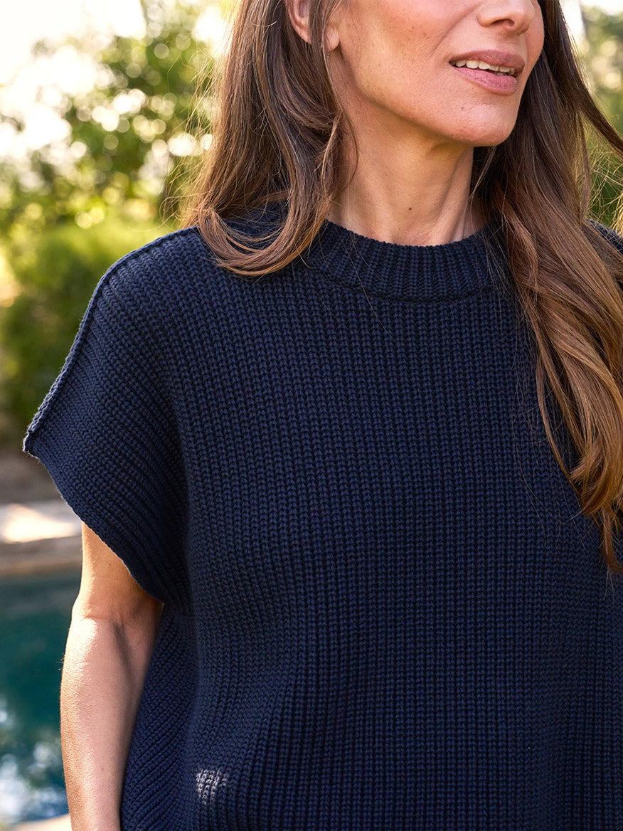 A person wearing a Frank & Eileen Montecito Italian Sweater Vest in Marine stands outdoors, with trees and a pool blurred in the background.