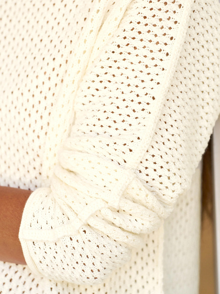 Close-up of a person wearing the Frank & Eileen Monterey Pointelle Rolled Funnel Neck Sweater in Ivory, featuring a cream-colored, long-sleeve design with rolled-up sleeves, crafted from luxurious Italian Pointelle fabric.
