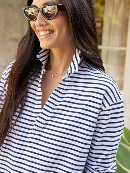 Woman smiling, wearing sunglasses and a Frank & Eileen Patrick Popover Henley in White/British Royal Navy Stripe Heritage Jersey, tropical plants softly blurred in the background.