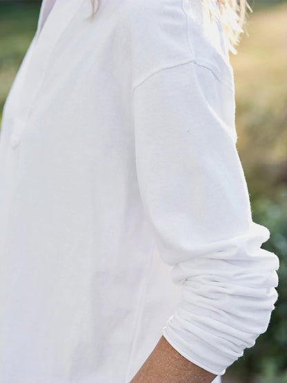 A close-up of a person wearing a Frank & Eileen Patrick Popover Henley in Vintage White Heritage Jersey, with the sleeve slightly pushed up, standing outdoors.