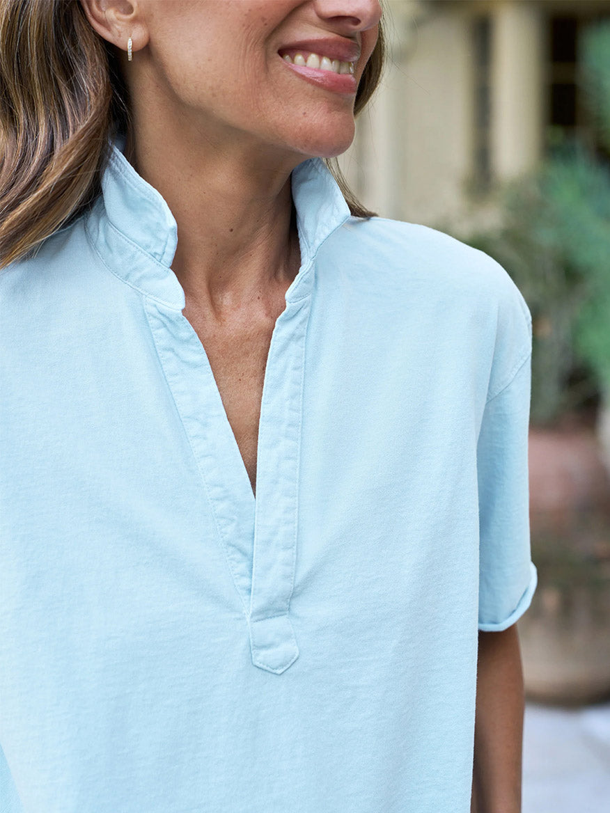A person wearing the Frank & Eileen Patty Short-Sleeve Popover Henley in Dive Blue Vintage Jersey smiles outdoors, with a softly blurred background.