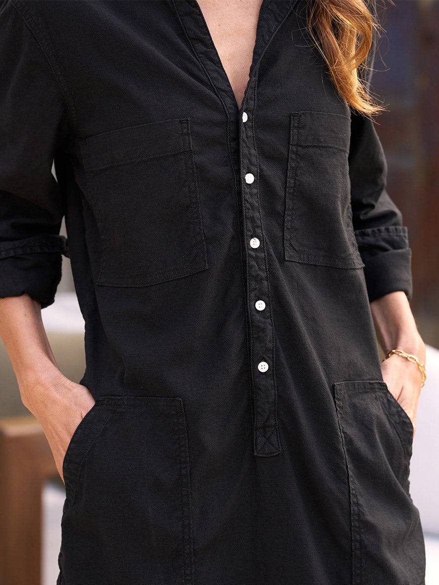 Wearing the Frank & Eileen Southern Ireland Utility Mini Dress in Black, a person blends flattering and functional style seamlessly, featuring rolled sleeves and hands resting in six handy pockets.