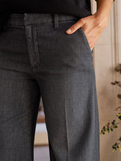 Close-up of a person wearing Frank & Eileen West Village NYC Wide-Leg Trouser in 1981 Wash, hand in pocket, standing indoors near a wall with plants.