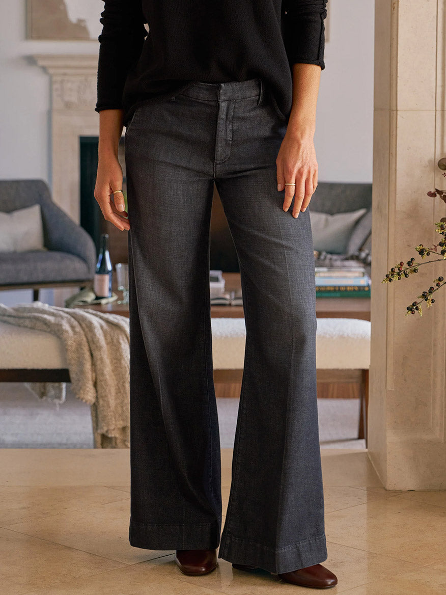 A person wears the Frank & Eileen West Village NYC Wide-Leg Trouser in 1981 Wash with a black top, standing on tiled floors in a living room setting.