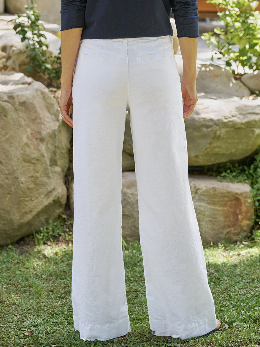 Outdoors on grass, a person faces away wearing the Frank & Eileen West Village NYC Wide-Leg Trouser in White and a navy long-sleeve top, with rocks and greenery creating a relaxed natural backdrop.