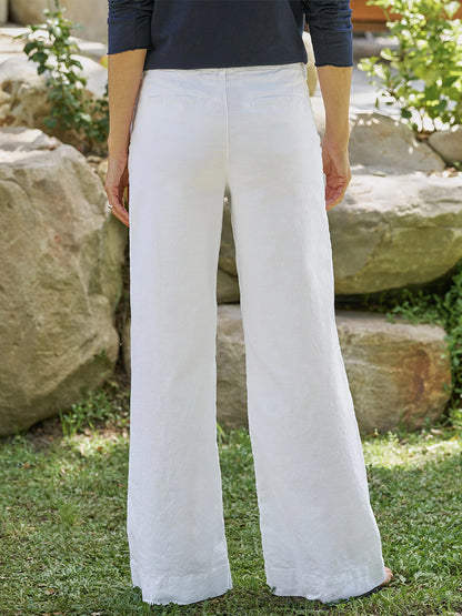 Outdoors on grass, a person faces away wearing the Frank & Eileen West Village NYC Wide-Leg Trouser in White and a navy long-sleeve top, with rocks and greenery creating a relaxed natural backdrop.