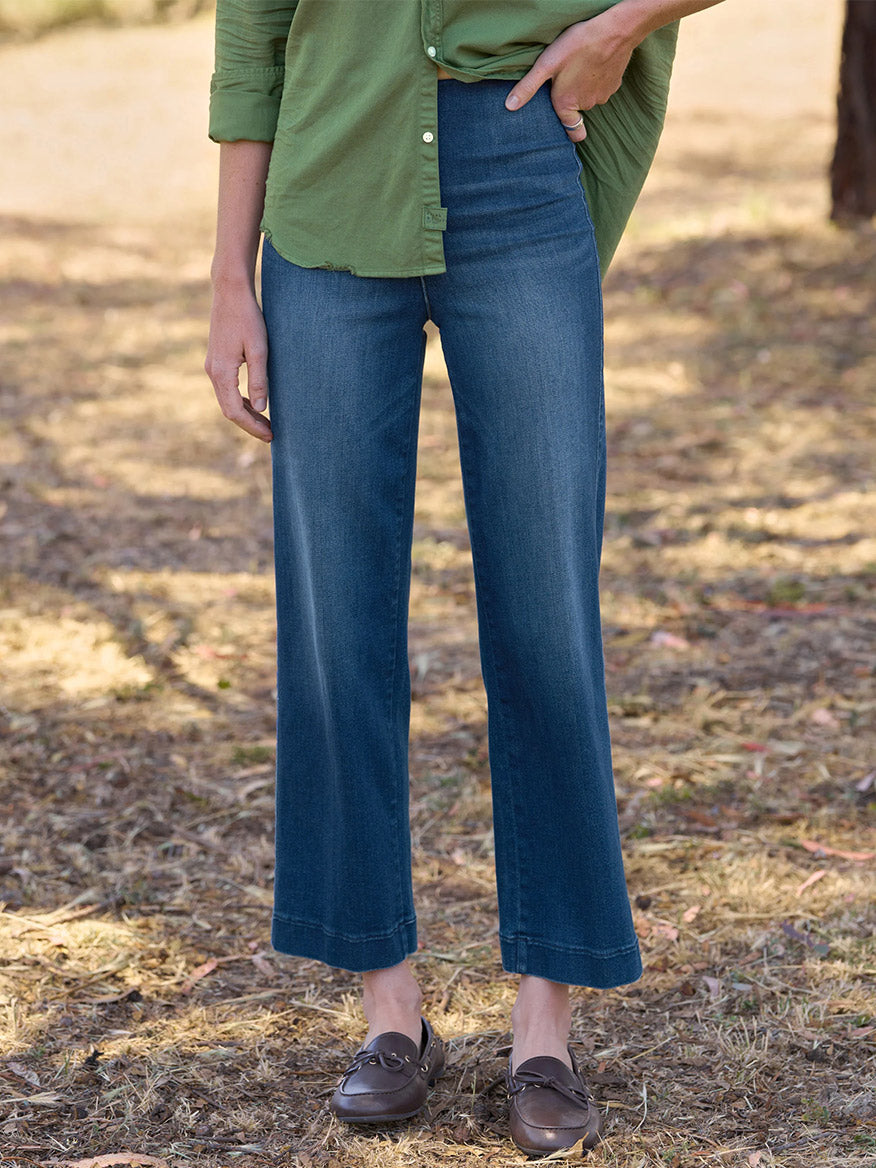 A person wearing a green shirt, Frank & Eileen Westport Illusion Wide-Leg Pull-On Jean in 1999 Wash, and brown loafers stands outdoors on dry grass. The wide-leg fit of the jeans adds a relaxed yet refined touch to the ensemble.