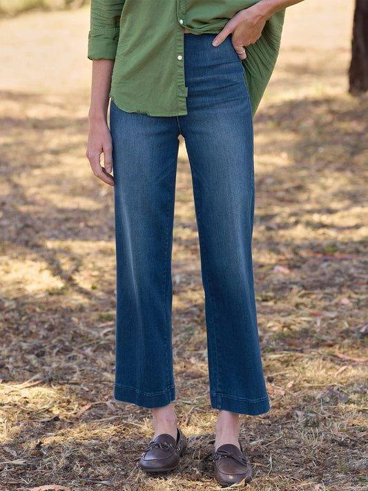 A person wearing a green shirt, Frank & Eileen Westport Illusion Wide-Leg Pull-On Jean in 1999 Wash, and brown loafers stands outdoors on dry grass. The wide-leg fit of the jeans adds a relaxed yet refined touch to the ensemble.