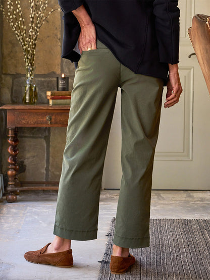 A person wearing a black top and Frank & Eileen Westport Italian Wide-Leg Chinos in Army stands indoors on a gray rug, with their back turned toward the camera.