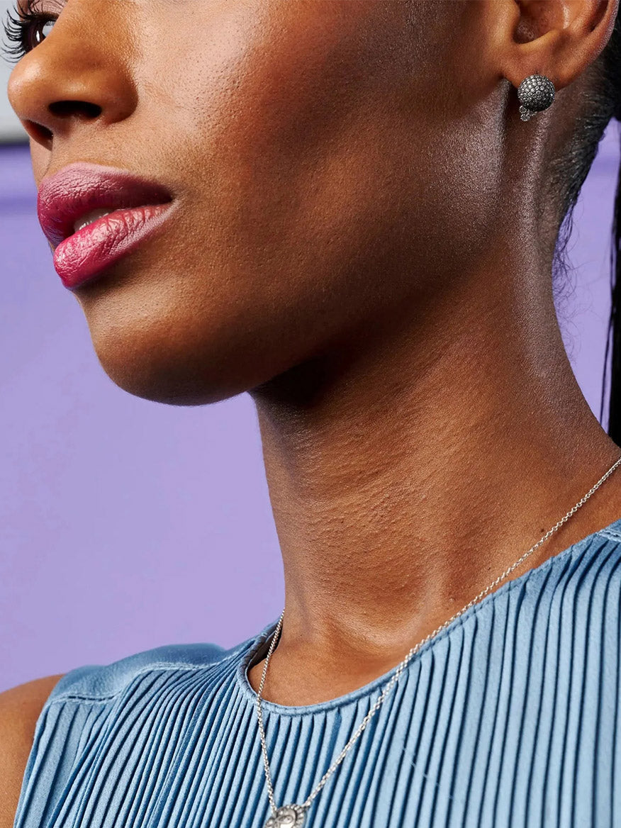 Close-up of a woman with pink lipstick and Freida Rothman Pavé Ball Stud Earrings in Black & Silver, showcasing her profile against a purple background.