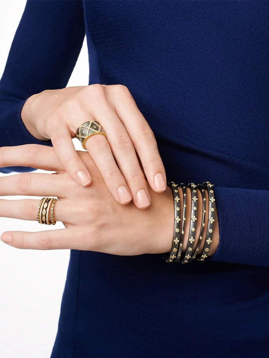 A woman's hands adorned with multiple Freida Rothman Thin Bezel Stacking Bangles in Black & Silver and rings, resting on her lap over a blue dress.