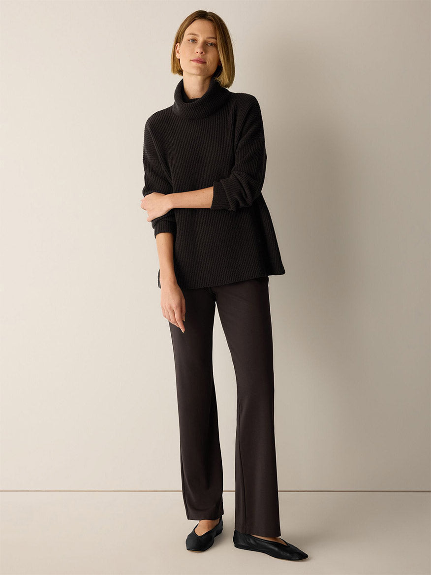 A person wearing a black turtleneck sweater, Eileen Fisher Extra-Fine Ponte Kick Pant in Coffee with a subtle flare, and black flats.