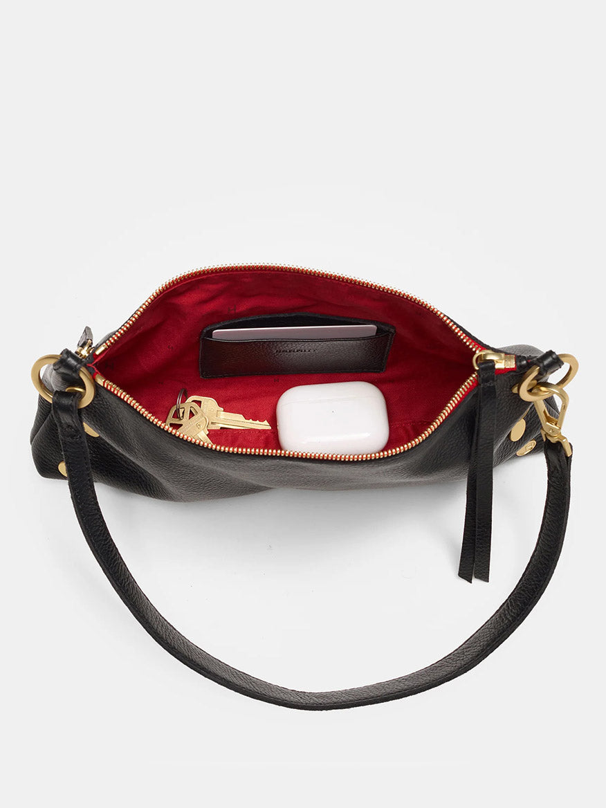 The Hammitt Los Angeles Kyle Shoulder Bag in Black/Brushed Gold & Red Zip is a versatile accessory crafted from black pebbled leather and featuring a striking red interior. It conveniently holds a wallet, set of keys, and white AirPods case. For added convenience and style, it includes an adjustable crossbody strap.