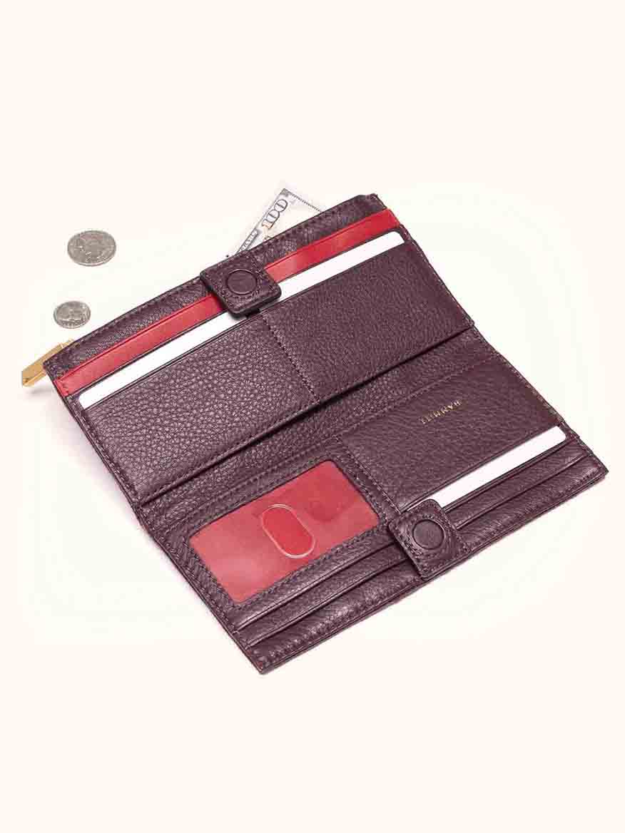 The Hammitt Los Angeles 110 North Wallet in Cabernet Pebble, an open leather folding wallet featuring a rich burgundy shade with red accents, is filled with cash and cards. Accompanied by loose coins, it comes equipped with numerous credit card slots for optimal organization.