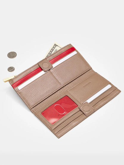 The Hammitt Los Angeles 110 North Wallet in Sculpted Taupe, an open beige folding wallet with red accents crafted from pebbled leather, holds cash and cards. It's beside three coins on a gray surface, highlighting its ample credit card slots.