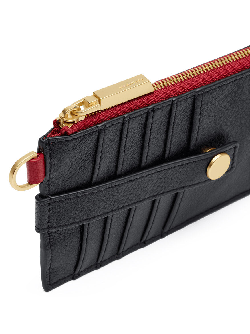 Close-up of the Hammitt Los Angeles 210 East Wallet in Black/Brushed Gold/Red Zip, crafted from black pebbled leather and accented with a brushed gold zipper, bold red lining, quilted stitching, a snap button strap, and a gold key ring attachment. This slim wallet with a D-ring attachment blends functionality and sophisticated style in every detail.