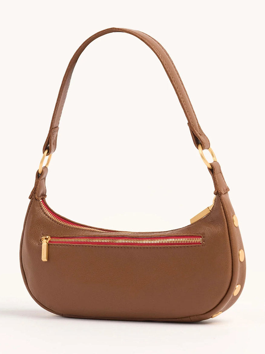 The Hammitt Los Angeles Becker Small in Mahogany Pebble is a brown leather handbag with a curved shape, featuring a red zipper pocket on the front, brushed gold hardware, and an adjustable shoulder strap for crossbody convenience.