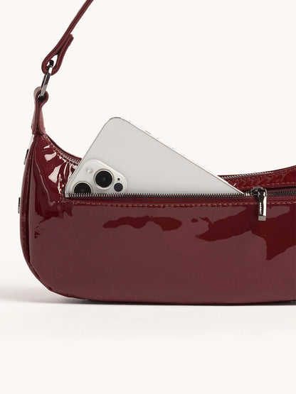 A Hammitt Los Angeles Becker Small in Pirouette Patent handbag, featuring a deep burgundy red hue of Italian patent leather, with a smartphone partially visible inside the zippered section.