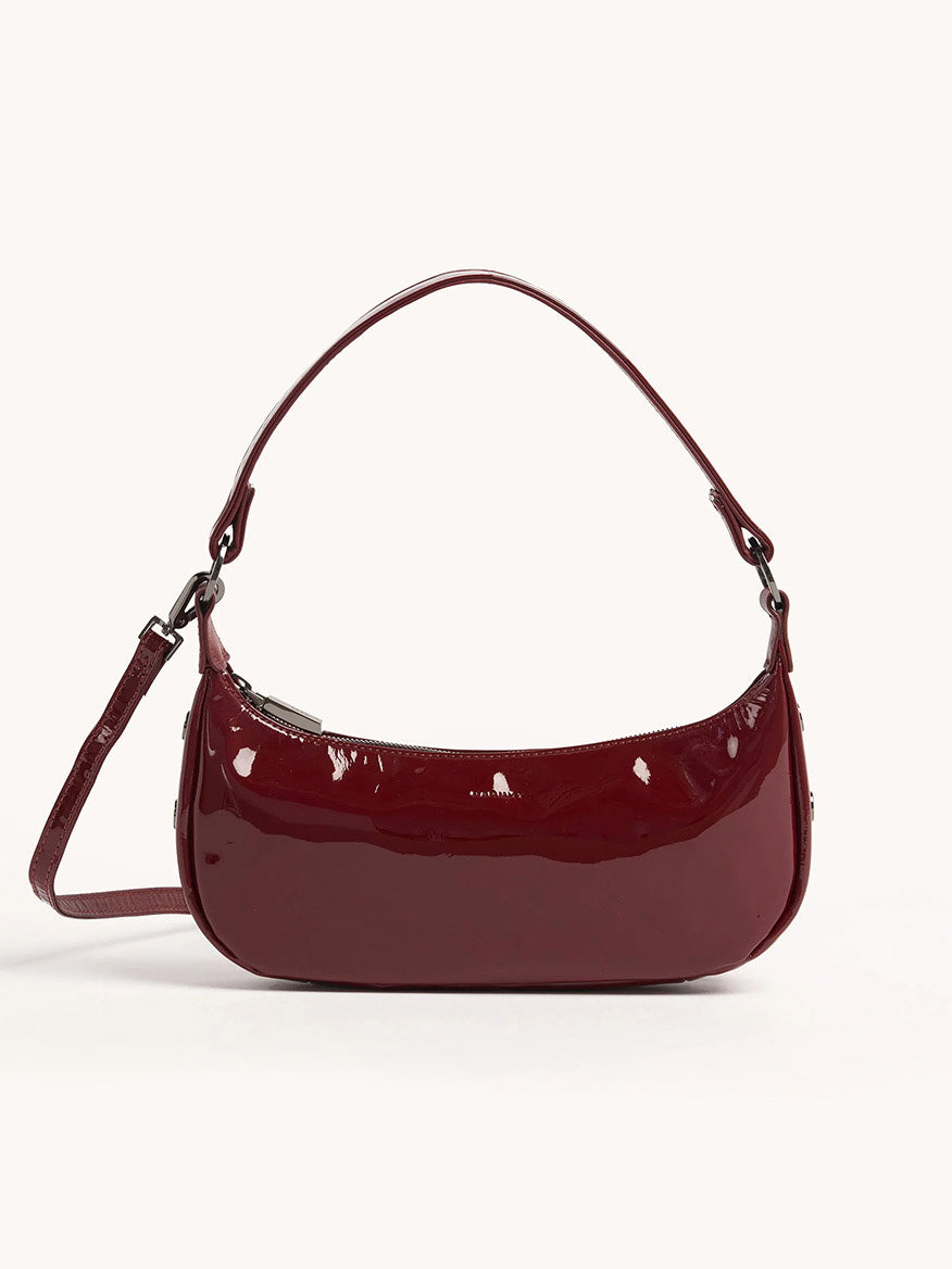 The Hammitt Los Angeles Becker Small in Pirouette Patent is a glossy handbag in a rich burgundy red hue, crafted from Italian patent leather. It features a short strap and a removable adjustable crossbody strap, set against a plain background.