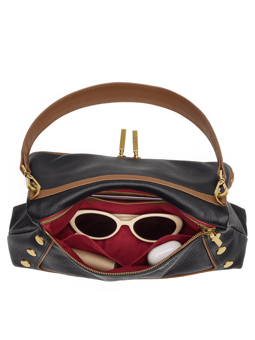 Display the Hammitt Los Angeles Beverly Medium in East End/Antique Gold, unzipped to reveal its red interior holding white sunglasses, a compact, and other small essentials. The black pebbled leather bag features a brown crossbody strap for an effortlessly chic look.