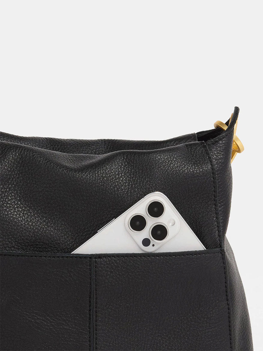 The Hammitt Los Angeles Bryant Large Crossbody Bag in Black & Brushed Gold features a black pebbled leather design with a white smartphone partially visible in its pocket and includes a sleek crossbody strap for effortless style.