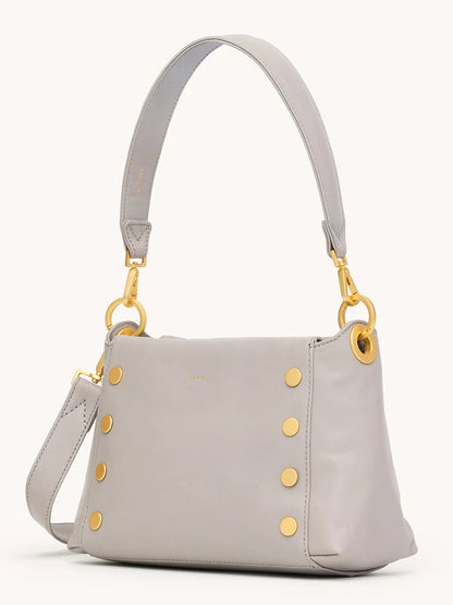 The Hammitt Los Angeles Bryant Medium Crossbody Bag in Stormy/Brushed Gold features light gray pebble leather, gold-tone hardware with six round studs, a wide shoulder strap, and an extra detachable strap for versatile wear.