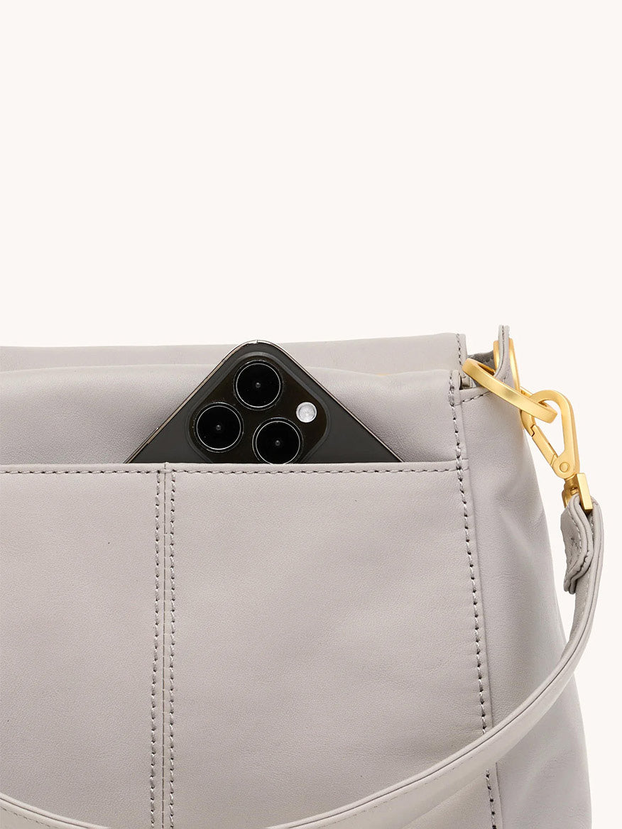 A black smartphone partially tucked into the front pocket of a Hammitt Los Angeles Bryant Medium Crossbody Bag in Stormy with brushed gold hardware.
